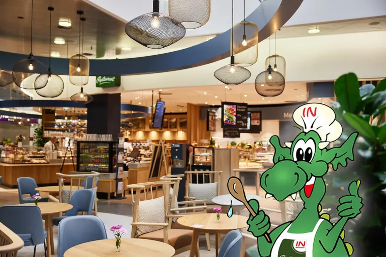 Moderner Food-Court mit Holztischen und blauen Stühlen, im Vordergrund ein grüner Cartoon-Drachenkoch, der einen Löffel in der Hand hält.