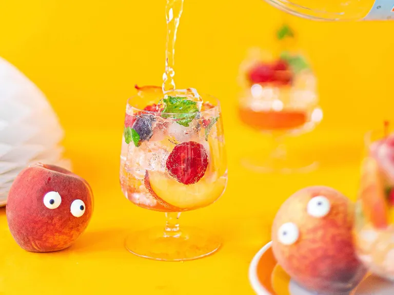 Hausgemachte Pfirsich-Holler-Limonade mit Erdbeeren, Heidelbeeren, Minze und Eiswürfeln im Glas