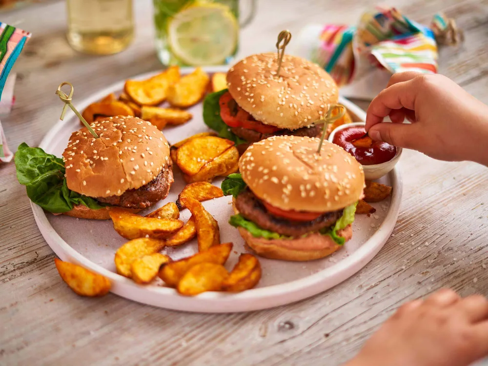 Drei Mini-Burger mit Kartoffelspalten und Ketchup auf einem Teller