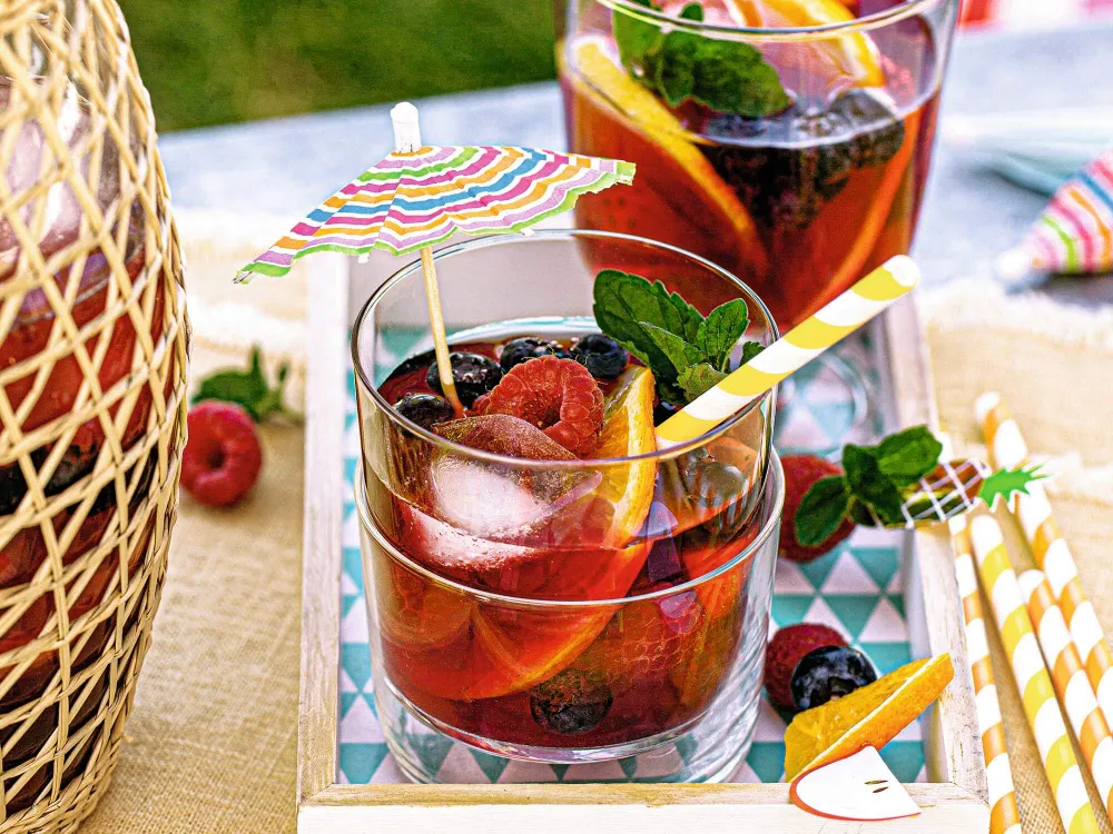 Alkoholfreie Sangria mit Beeren, Orange, Minze und Eiswürfeln in dekorierten Gläsern