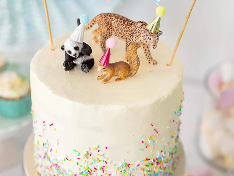 Weiße Geburtstagstorte mit Tierfiguren, Partyhüten und bunten Zuckerstreuseln