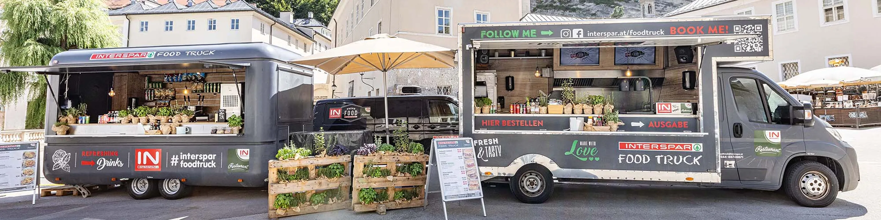 Der INTESPAR Foodtruck stehen nebeneinander und bieten unter bunten Sonnenschirmen frische Getränke und Speisen an