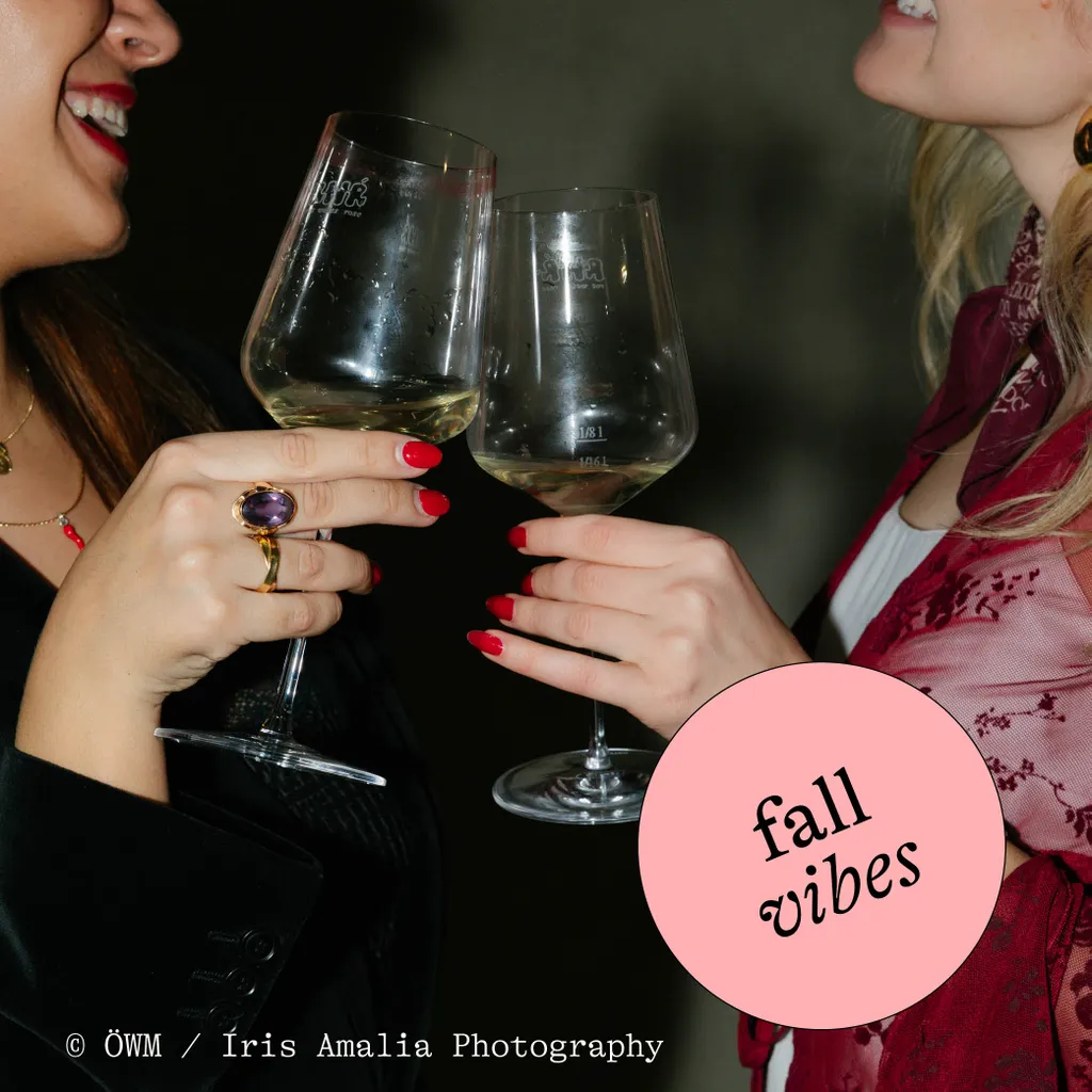 Two people toasting with wine glasses, both with red nails and wearing stylish attire. A pink circle says "fall vibes" in the corner.
