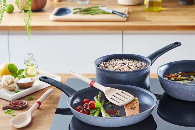 Unterschiedliche Pfannen der Marke Tefal, die auf einem Induktionsherd in einer Küche stehen und es werden gerade unterschiedliche Gerichte gekocht, wie Lachs, Gemüsebeilagen uvm.