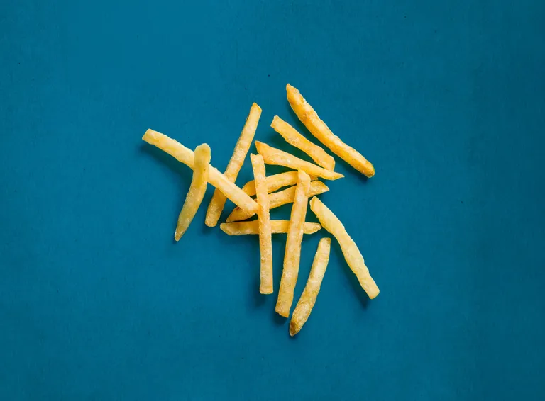 Ein verstreuter Haufen goldgelber Pommes frites auf einem leuchtend blauen Hintergrund.