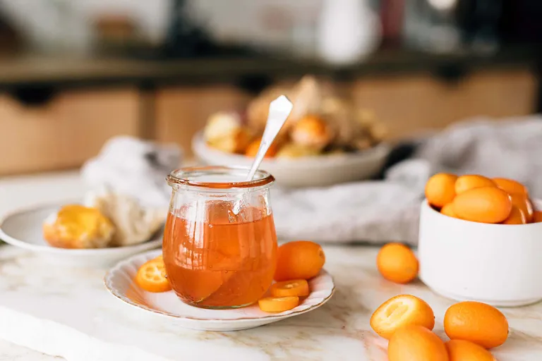 Selbst gemachte Kumquatmarmelade im Glas mit frischen Kumquats auf einem hell gedeckten Tisch