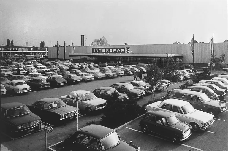 Außenansicht eines alten INTERSPAR-Hypermarktes in schwarz-weiß mit einem großen Parkplatz und vielen parkenden Autos