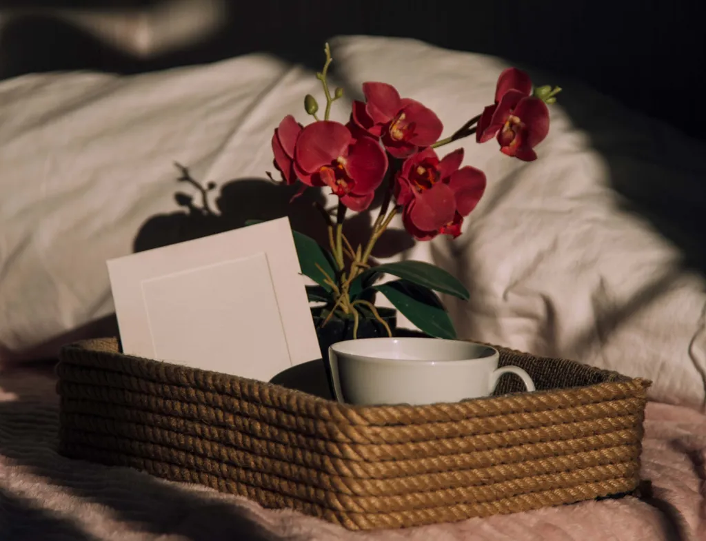 Geschenkkorb mit roter Orchidee, Tasse und Grußkarte auf einer Decke