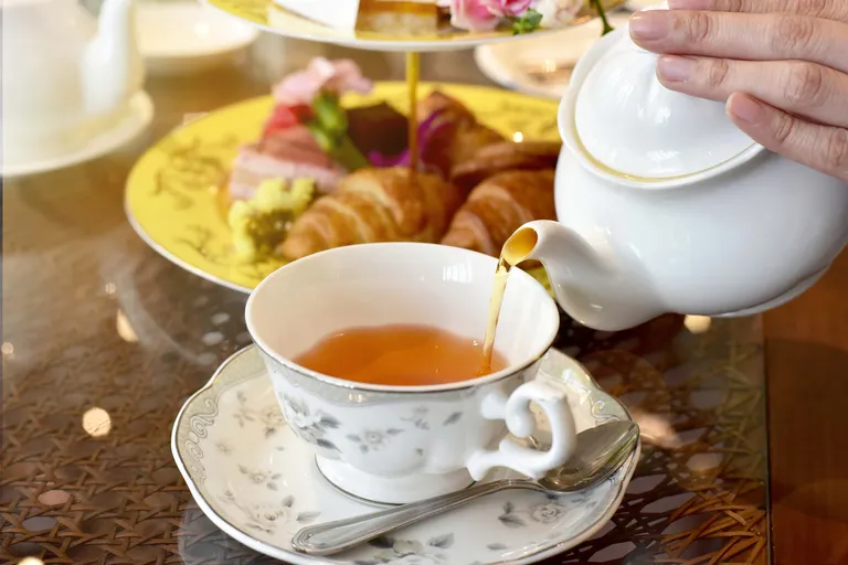 Tee wird aus einer Porzellankanne in eine klassische Teetasse beim Nachmittagskaffee eingeschenkt