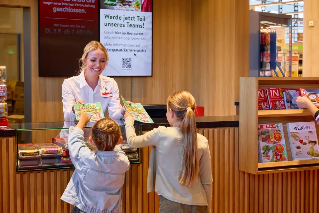 Mitarbeiterin überreicht Kindern das INGO-Kindermagazin an der Information im INTERSPAR Markt