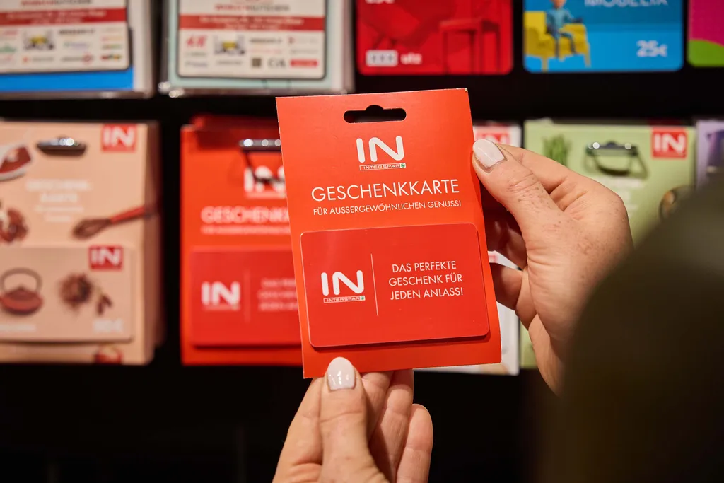 Hände, die ein rotes Geschenkkartenpaket mit deutschem Text halten, umgeben von verschiedenen anderen bunten Geschenkkartenauslagen.