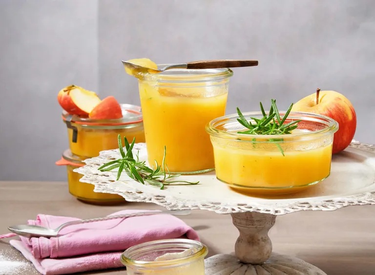 Cremiges Apfelmus mit Rosmarin in Gläsern auf einer Etagere mit frischen Äpfeln