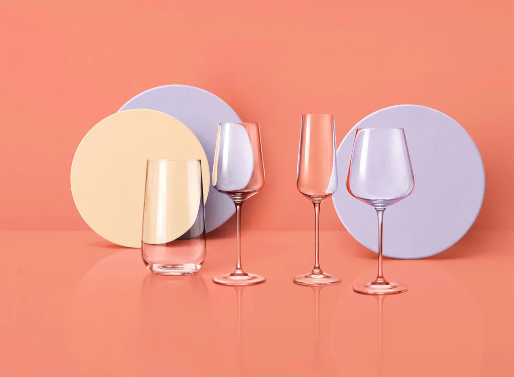 Mehrere verschiedene Glas-Produkte wie Weingläser, Wassergläser und Teller von Spiegelau vor einem lachsfarbenen Hintergund