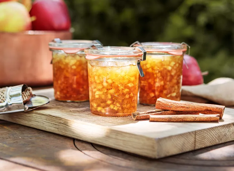 Hausgemachte Apfelmarmelade mit Zimt in Einmachgläsern auf einem Holzbrett mit Äpfeln und Zimtstangen