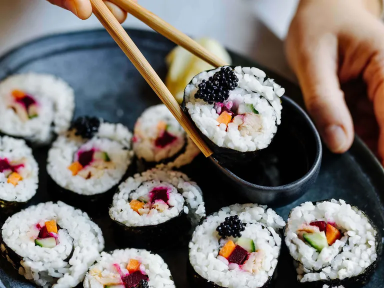 Frische Maki-Sushi mit Gemüse und Kaviar werden mit Essstäbchen serviert