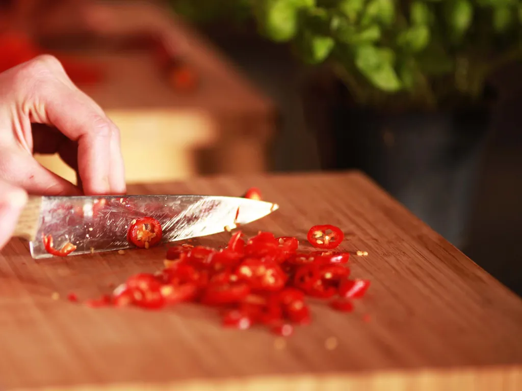 Frische rote Chilischoten werden auf einem Holzbrett mit einem Küchenmesser geschnitten