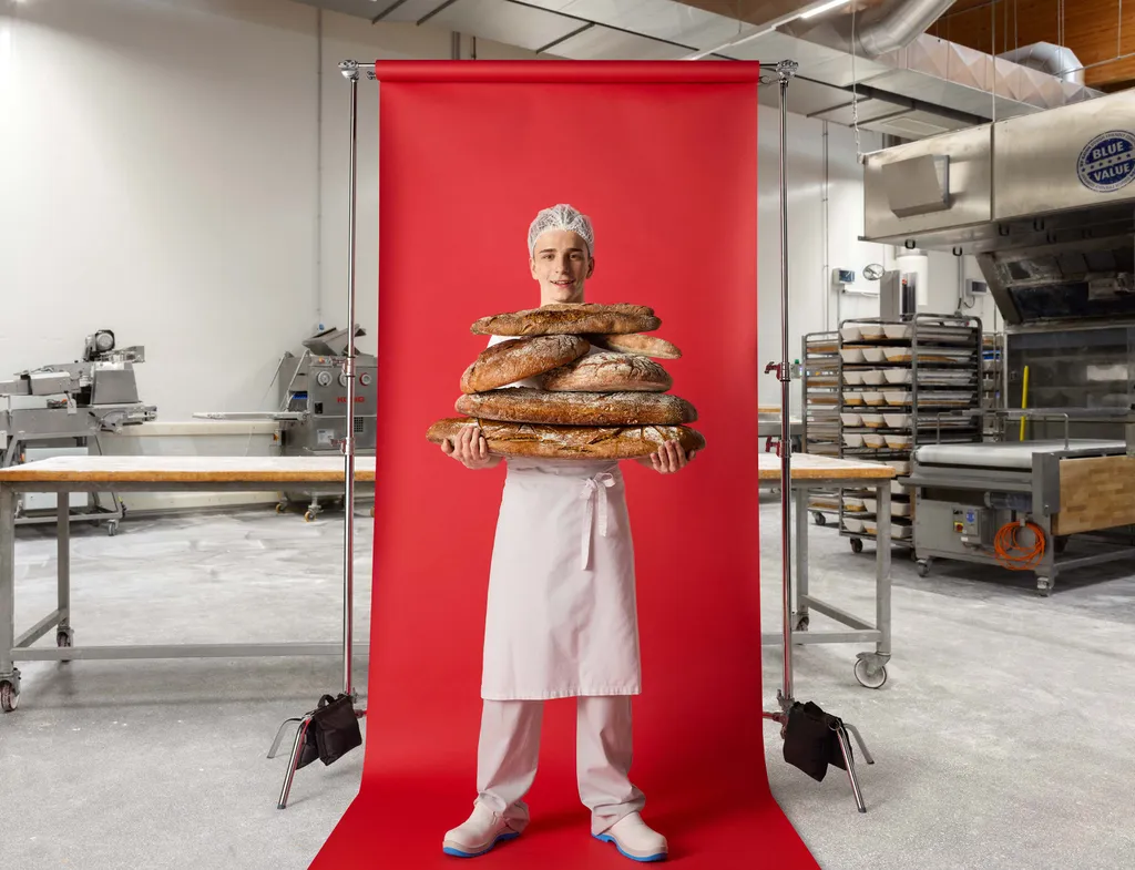 Bäckerei-Lehrling hält mehrere frisch gebackene Brote vor rotem Hintergrund