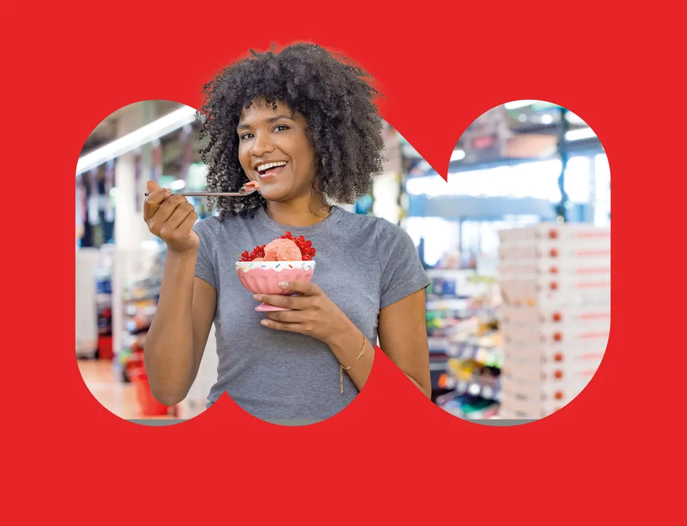 Lachende Kundin genießt Eis aus einem Eisbecher im INTERSPAR Markt
