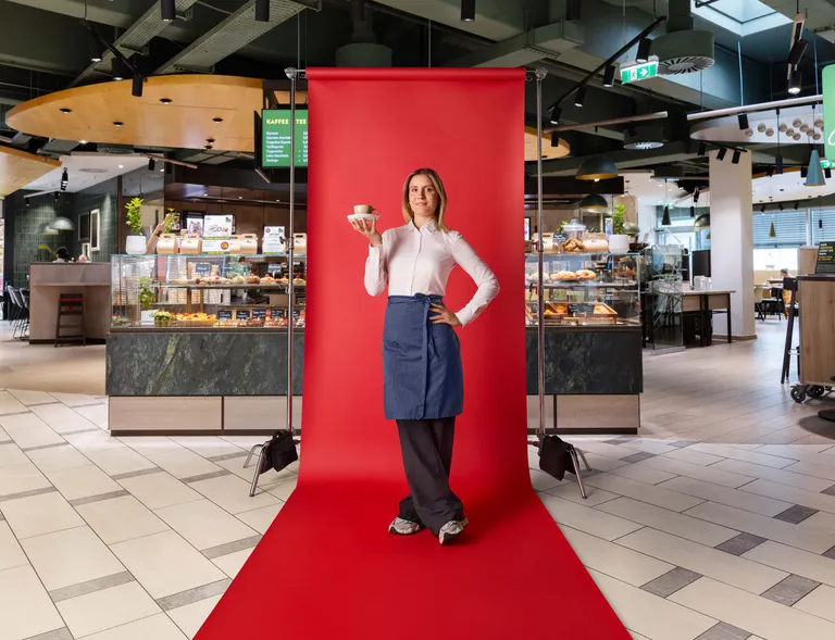 Lehrling im Gastronomiebereich präsentiert eine Tasse Kaffee vor rotem Fotohintergrund