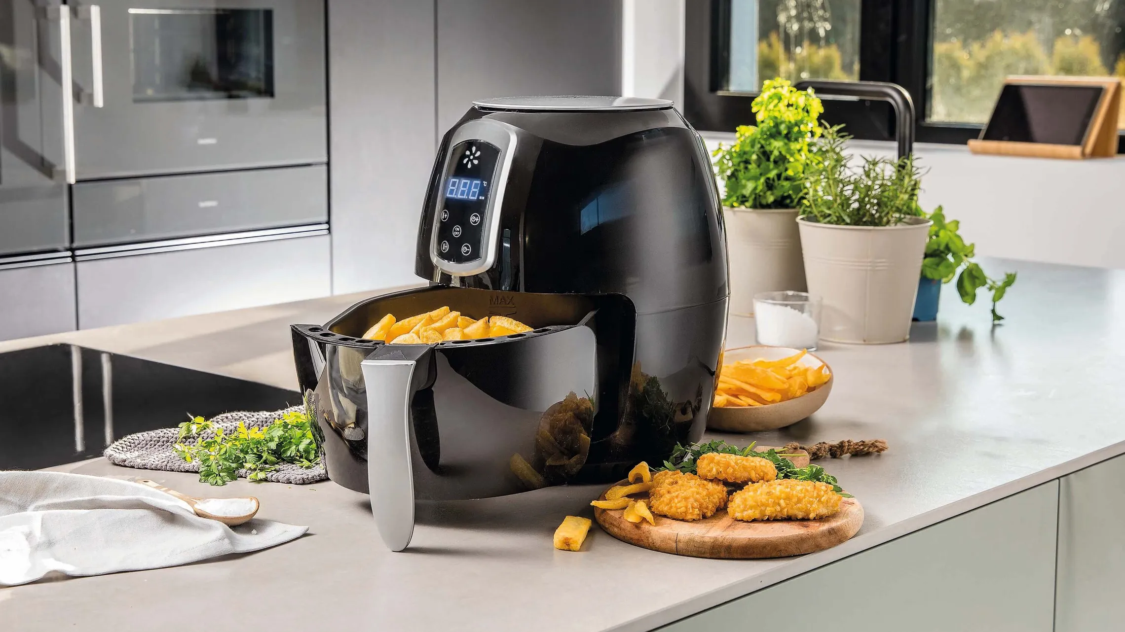 Moderne Heißluftfritteuse in einer Küche mit knusprigen Pommes und panierten Snacks auf der Arbeitsfläche