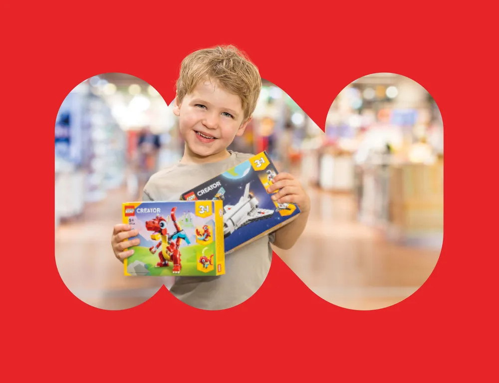 Lachendes Kind hält LEGO Creator Spielzeug im INTERSPAR Markt