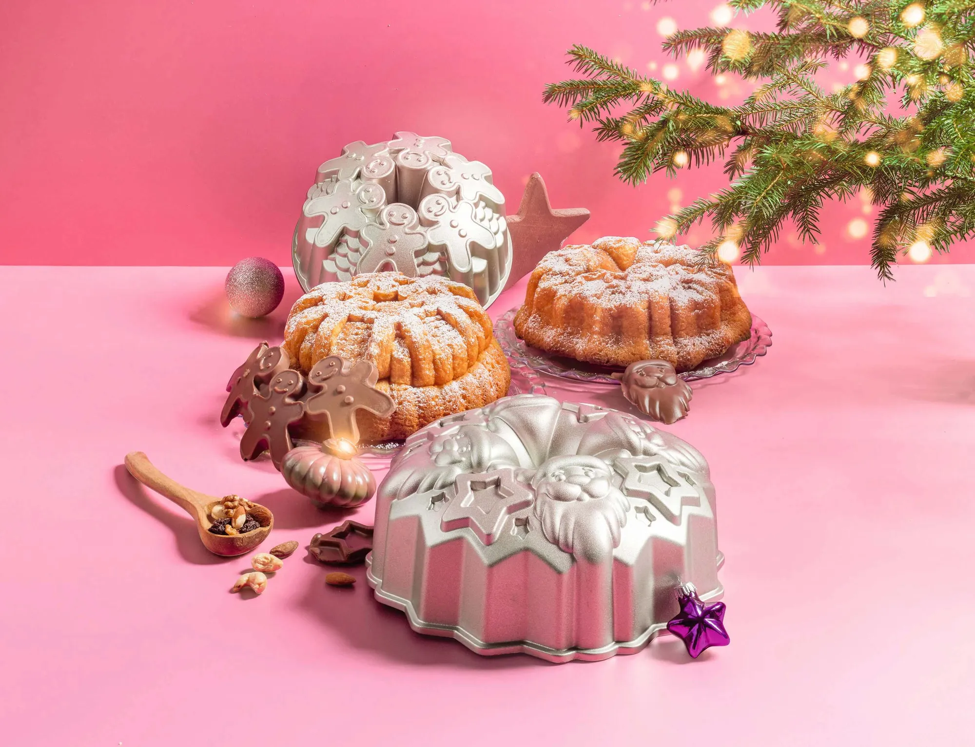 Mehrere Gugelhupfformen mit Mustern und Motiven und zwei frisch gebackene Gugelhupf auf einem rosa Tisch