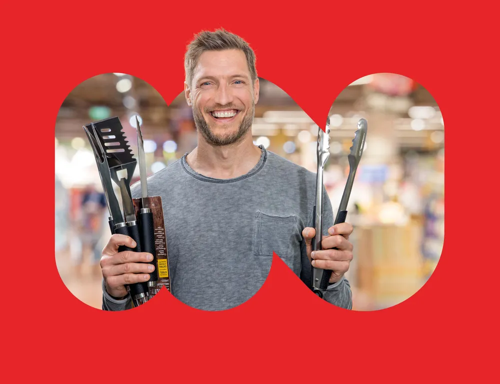 Lachender Mann präsentiert Grillzubehör und Grillzangen im INTERSPAR Markt