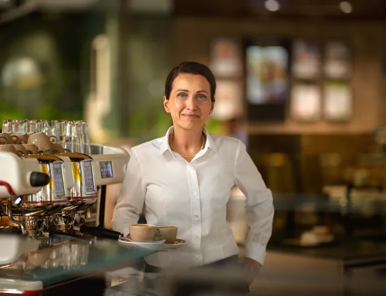 Mitarbeiterin im INTERSPAR-Restaurant steht mit Kaffee an der Kaffeemaschine