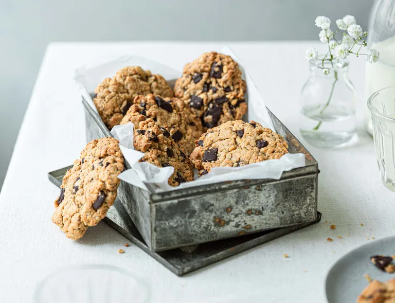 Frisch gebackene Schoko-Erdnuss-Cookies in einer grauen Metallschale auf Backpapier
