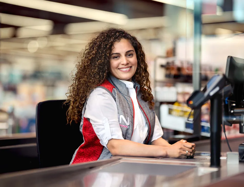 Mitarbeiterin von INTERSPAR sitzt lächelnd an einer Kassa im Hypermarkt
