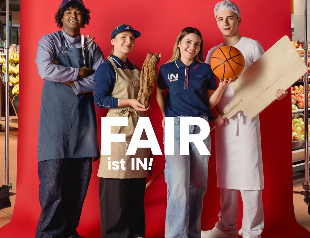 Vier junge INTERSPAR Mitarbeitende mit Brot, Basketball und Arbeitsutensilien vor rotem Hintergrund mit dem Schriftzug „Fair ist IN!“