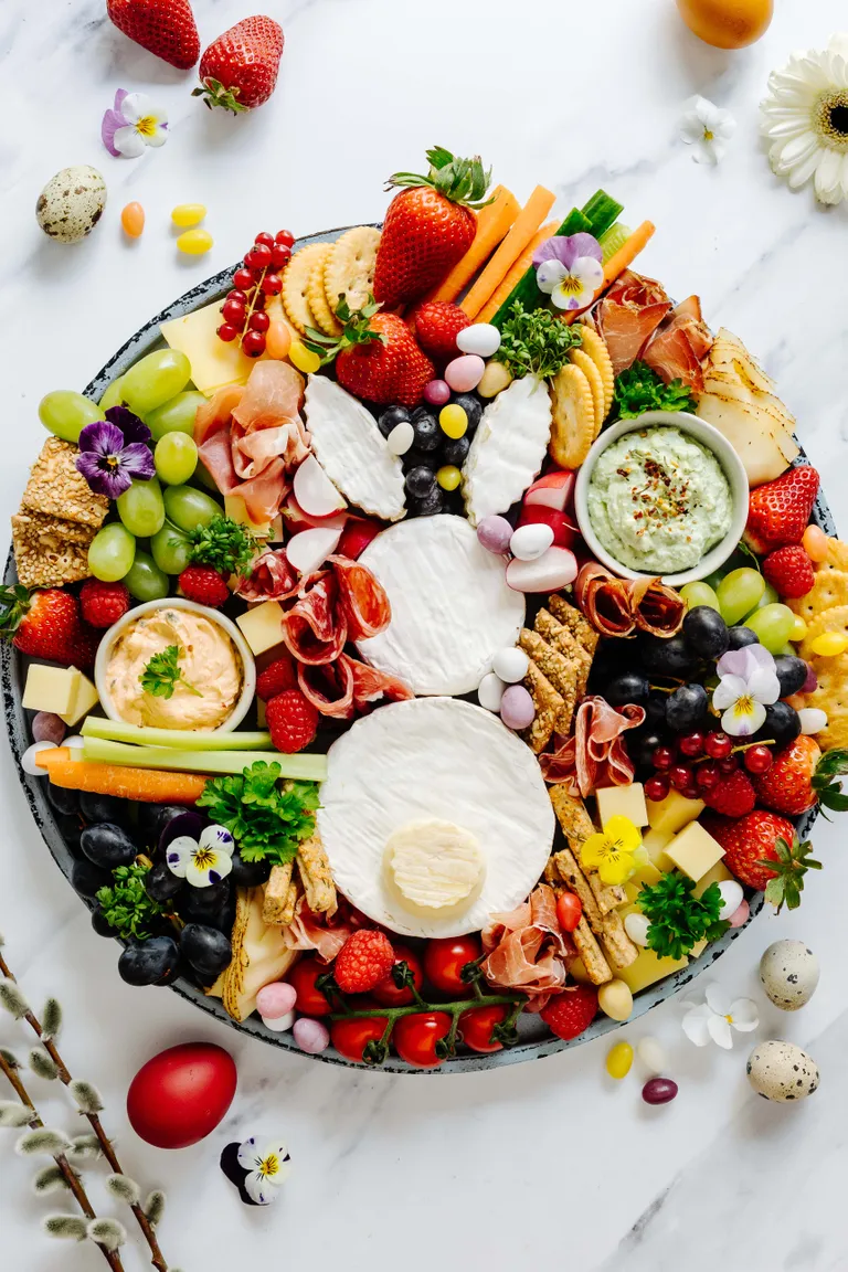 Eine festliche Wurst- und Käseplatte mit Käse, Obst, Gemüse, Crackern, Fleisch, Dips und bunten Dekorationen, ansprechend und farbenfroh angerichtet.