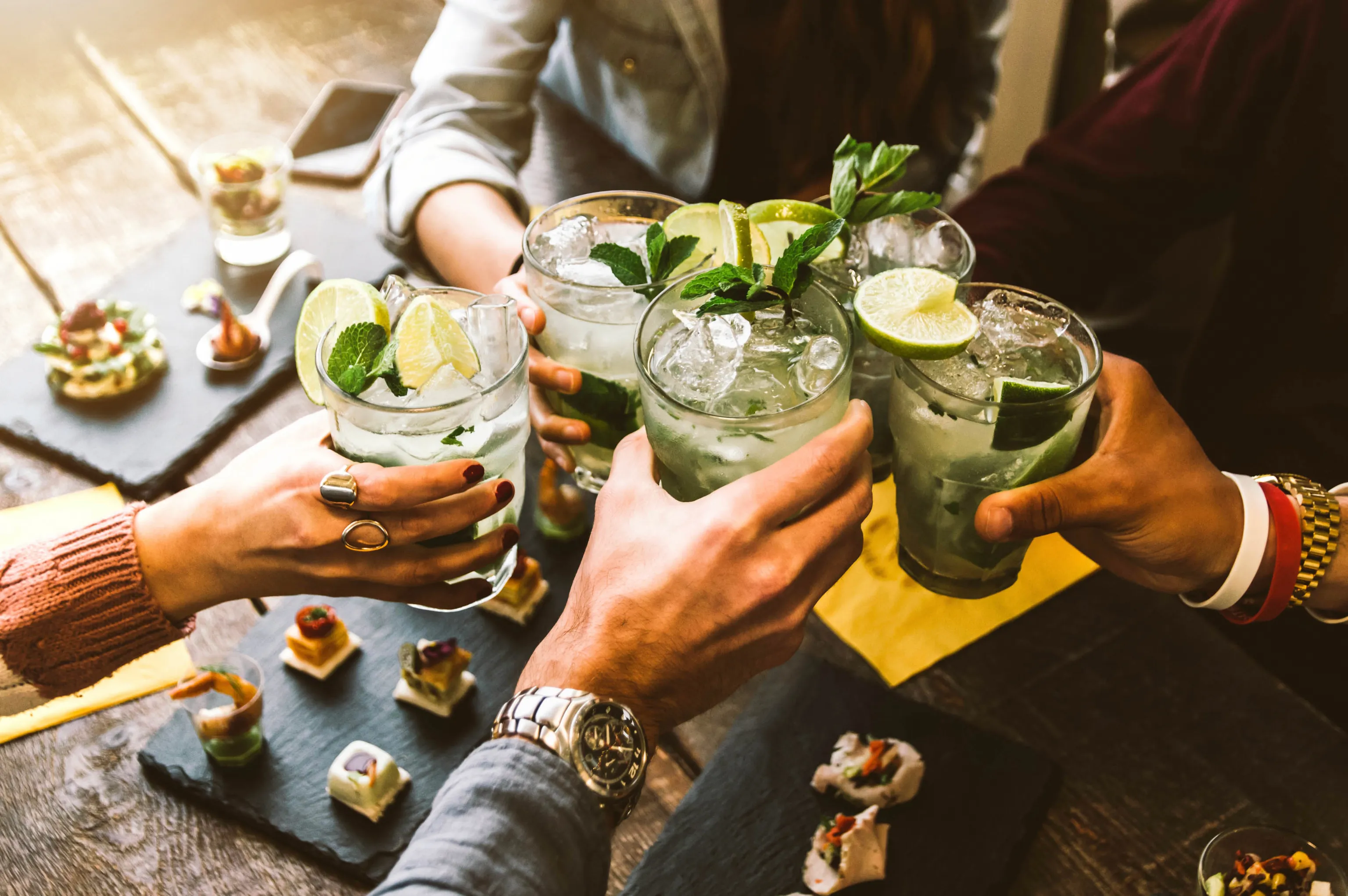 Eine Gruppe von Menschen, die an einem Tisch mit Häppchen mit Mojitos anstoßen.