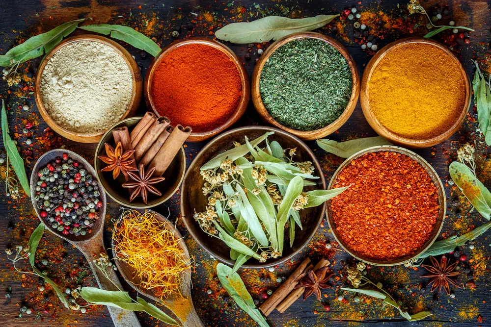 Mehrere Schalen voller verschiedener Gewürze wie Anis, Zimtstangen, Chili, Kurkuma, etc.