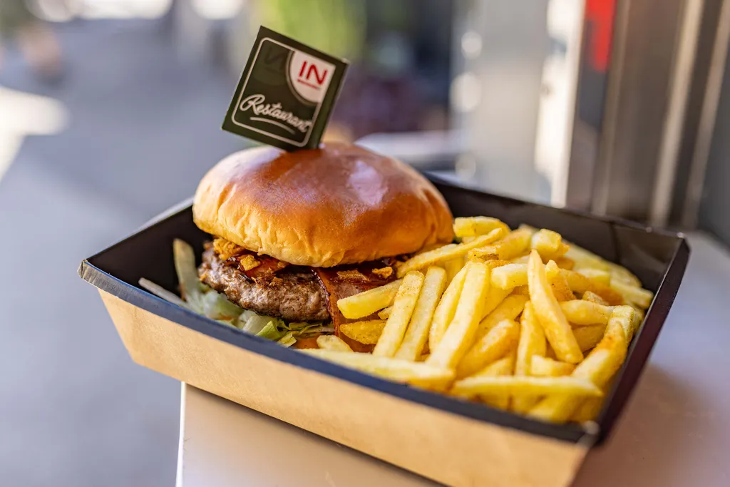 Burger mit knusprigem Speck und Salat im Brötchen, serviert mit goldbraunen Pommes frites in einer Pappschale, garniert mit einer kleinen Fähnchen.