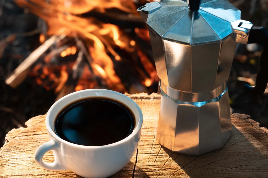 Tasse Kaffee und italienische Mokkakanne neben einem offenen Feuer