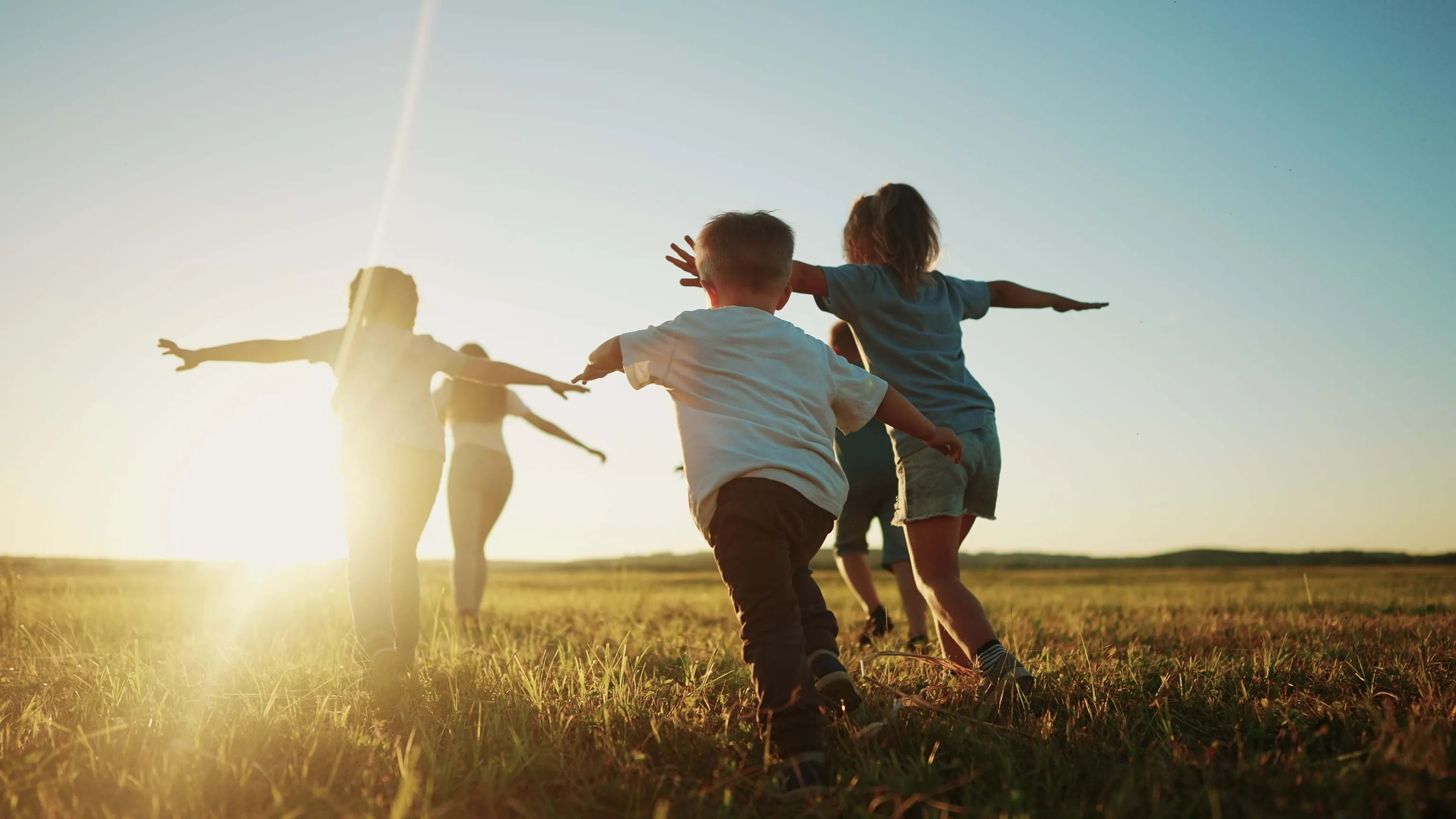 Kinder laufen und spielen gemeinsam auf einer Wiese bei Sonnenuntergang