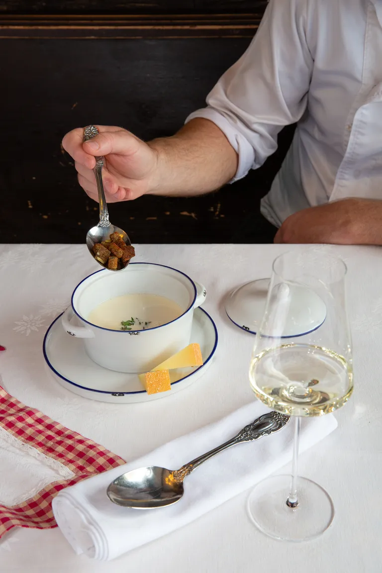 Bergkäsesuppe mit Almbrotcroutons, serviert mit einem Glas Weißwein am gedeckten Tisch