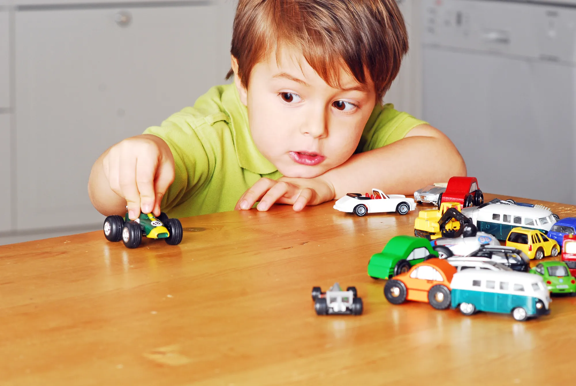 Junge in grünem T-Shirt spielt mit Spielzeugautos am Holztisch