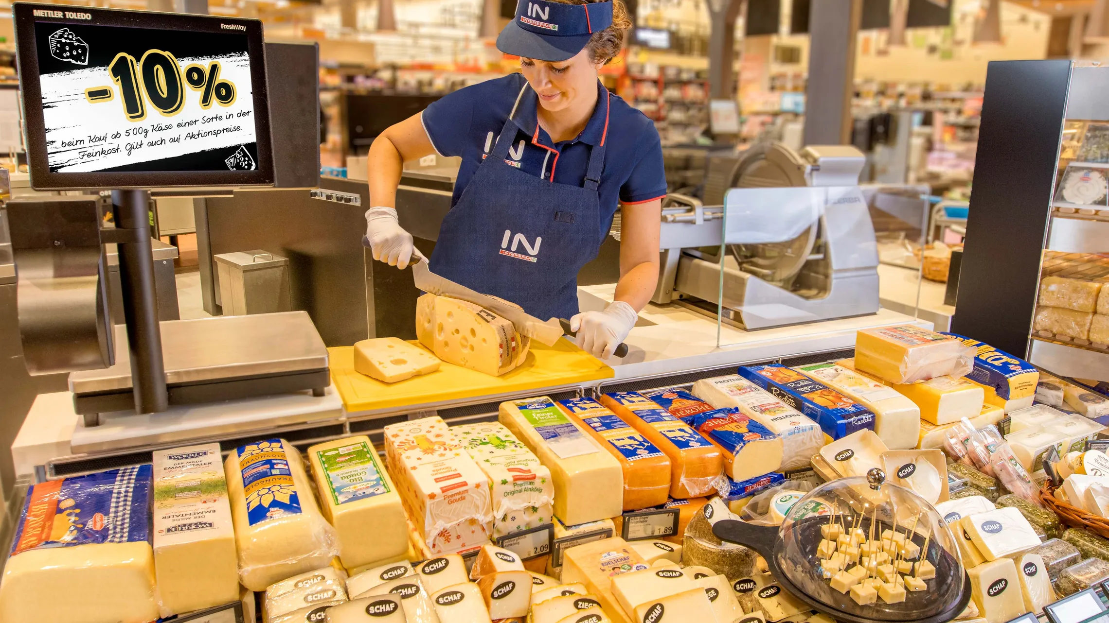 Eine Mitarbeiterin portioniert Käse an der Käsetheke