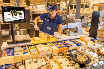 Eine Mitarbeiterin portioniert Käse an der Käsetheke
