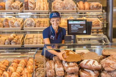Eine Mitarbeiterin legt einen Laib Brot in die Vitrine der Brotabteilung