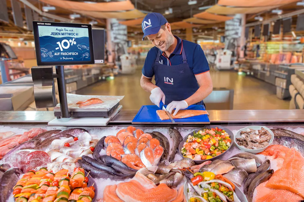 Ein Mitarbeiter portioniert frischen Fisch an der Fischtheke