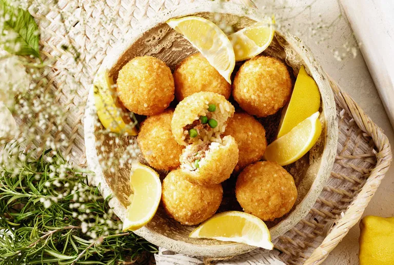 Goldbraune sizilianische Arancini mit herzhafter Reisfüllung und Zitronenspalten