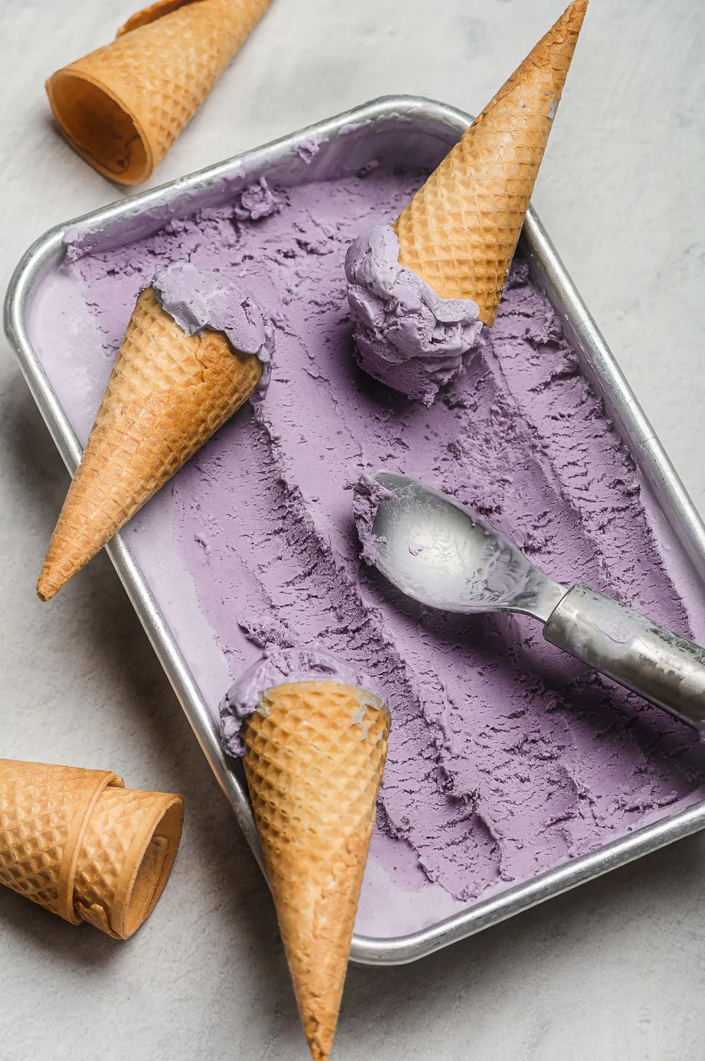 Ein Behälter mit lila Eiscreme und mehreren Eistüten