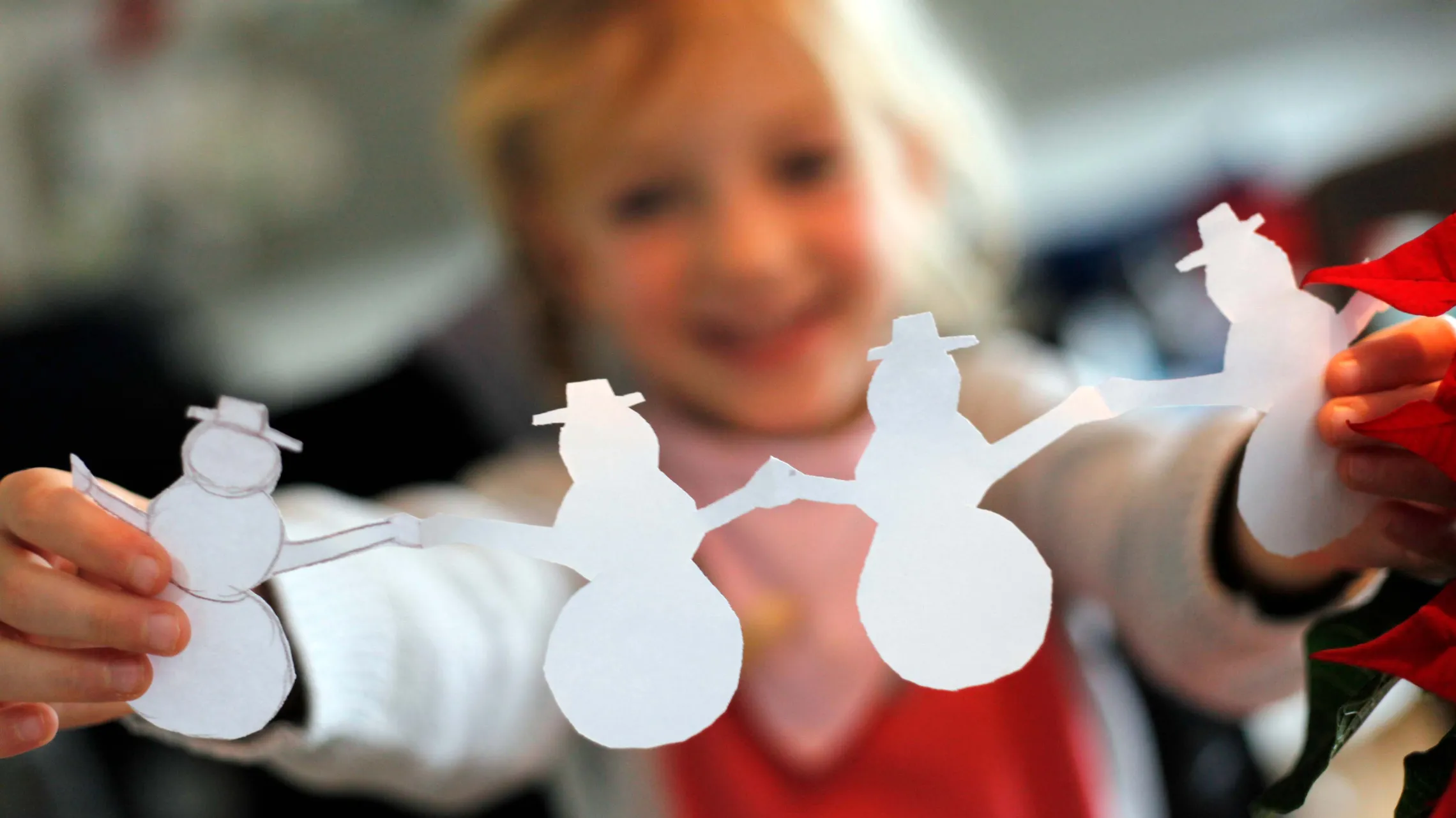 Kind hält selbst gebastelte Schneemänner aus Papier als weihnachtliche Dekoration
