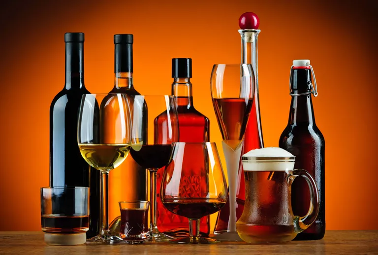 Eine Auswahl an alkoholischen Getränken, darunter Wein, Spirituosen und Bier, angerichtet in Flaschen und Gläsern vor einem warmen orangefarbenen Hintergrund.
