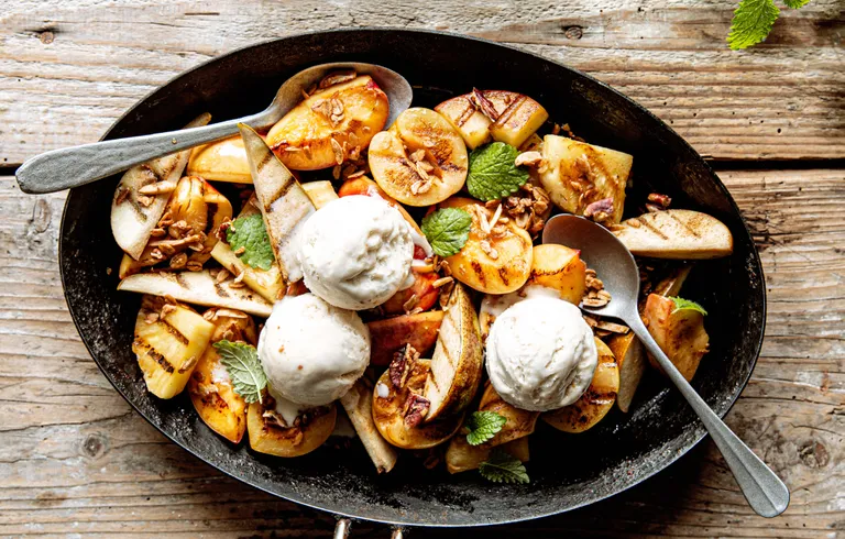 Gegrilltes Obst mit Vanilleeis, Nüssen und frischer Minze in einer gusseisernen Pfanne