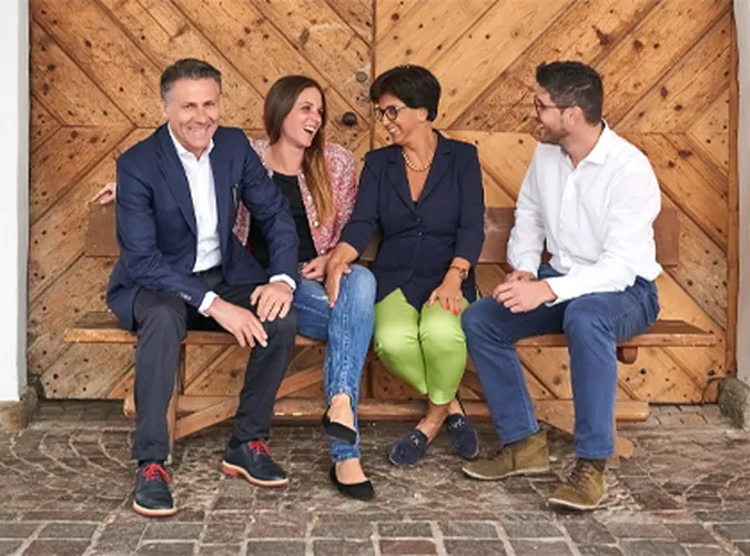 Vier Menschen sitzen auf einer Bank vor einer Holztür, lächeln und unterhalten sich ungezwungen miteinander.