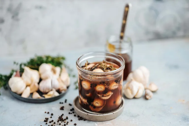 Eingelegte Knoblauchzehen mit Kräutern und Pfefferkörnern im Glas